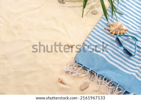 Top view of striped blue towel with sunglasses on sandy beach. Background with copy space and visible sand texture.