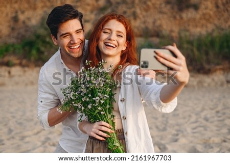 Young couple family man woman wear white clothes hug rest together hold bouquet do selfie shot mobile cell phone post photo social network at sunrise over sea sand beach outdoor seaside in summer day