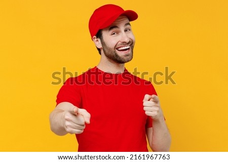 Professional delivery guy employee man in red cap T-shirt uniform workwear work as dealer courier point index finger camera on you say do it isolated on plain yellow background studio Service concept