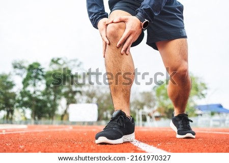 Young man runner has sore knee because he ran too long. Male Exercising until the injury. Overtrained. Young sport man accident running on track Royalty-Free Stock Photo #2161970327