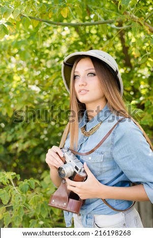 Young beautiful woman in pith hat taking pictures on retro camera on green trees summer copy space background