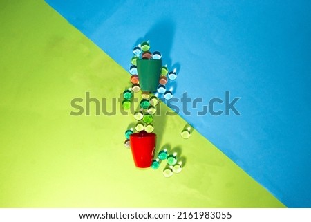 green and red small drinking glass full of beads spilling around on a green-blue background, creative party design