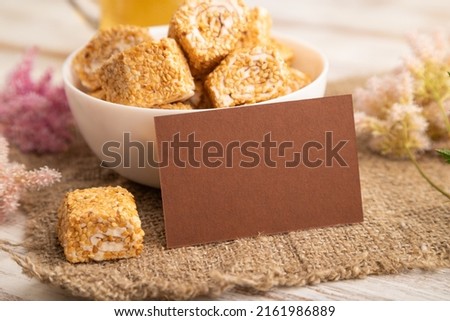 Brown business card with traditional turkish delight (rahat lokum) in white ceramic bowl on a white wooden background. side view, close up.