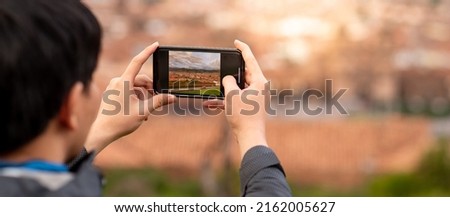 Asian man tourist taking a photo of cusco city on smartphone camera. Cusco (Cuzco) is a city in southeastern Peru, near the Urubamba Valley of the Andes mountain range