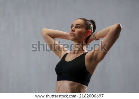 Young sporty woman in sports clotheswith arms behind head against beige background, copy space