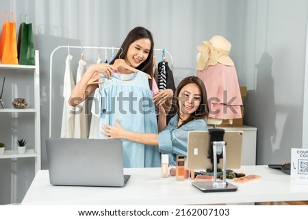 Asian woman friends couple talk to camera to sell the clothes at home. Young attractive business people female live streaming and showing clothing to customer in online retail to sales at office store