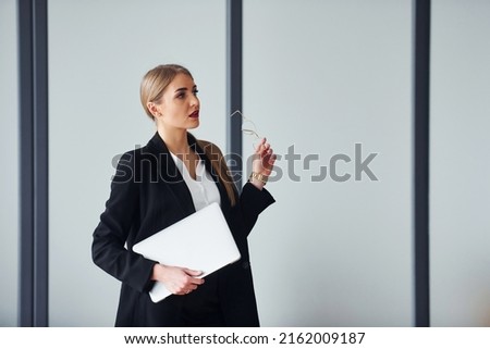 Standing against grey background. Young adult woman in formal clothes is indoors in the office.