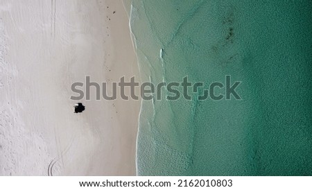 Aerial picture. Car on the beach, view from the sky.  Shallow clear water and white sand. Off-road adventure in Australia.