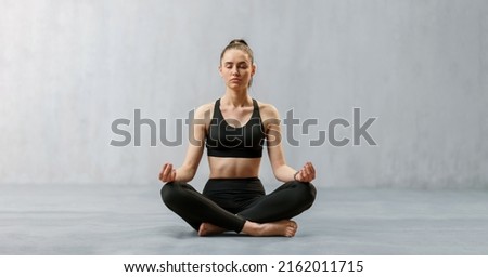 Young healthy woman in black sportsclothes practising yoga in studio, in a yoga position, copy space Royalty-Free Stock Photo #2162011715
