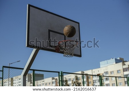 Ball over basketball hoop placed on sports ground on background of blue sky in city in summer 