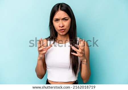 Young hispanic woman isolated on blue background upset screaming with tense hands.