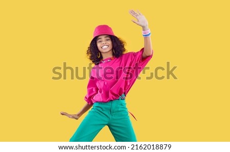 Happy joyful Black kid in funky outfit dancing in studio. Cheerful African dancer girl wearing loose fuchsia top, bucket hat and green pants enjoying hype and having fun. Children's fashion concept Royalty-Free Stock Photo #2162018879