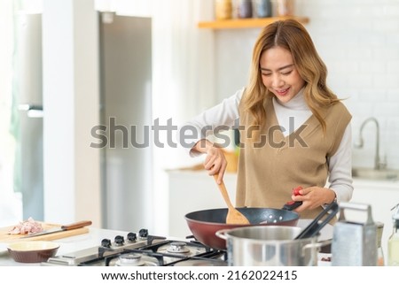 Young beautiful Asian woman enjoy cooking healthy food fried pasta on cooking pan in the kitchen at home. Happy female having dinner party meeting celebration with friends on holiday vacation Royalty-Free Stock Photo #2162022415