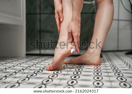 Close up of woman in bathroom applying moisturizing cream on heels Royalty-Free Stock Photo #2162024317