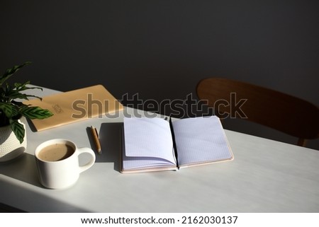 Aesthetic home office desk table. Feminine workspace with paper notebook, cup of coffee, plant, chair in sunlights Royalty-Free Stock Photo #2162030137