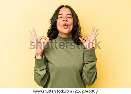 Young hispanic woman isolated on yellow background relaxes after hard working day, she is performing yoga.