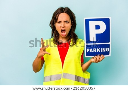 Young hispanic woman holding parking placard isolated on blue background