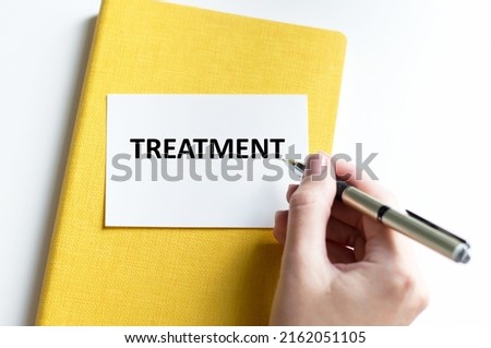 Treatment inscription on a white card that lies on a yellow notebook on a white table next to the doctor's hand