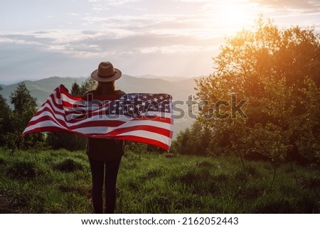 Silhouette of young girl in hat holding American Flag looking out at landscape. Patriotic american woman 20s old years enjoying nature during summer weekend. July 4th forth independence day concept Royalty-Free Stock Photo #2162052443