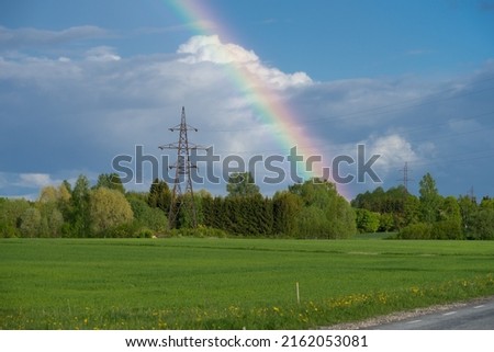Half rainbow over green field. Grey clouds over the colorful arc. Meteorological phenomenon that is caused by dispersion of light in water droplets resulting in a spectrum. Spring evening in Estonia. Royalty-Free Stock Photo #2162053081