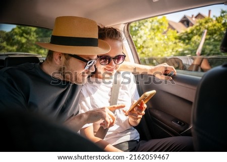 Young cheerful happy couple of travelers sitting in car looking at smartphone screen, travel comfort safety taxi concept Royalty-Free Stock Photo #2162059467