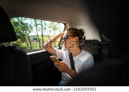 Young woman with a smartphone in her hands while sitting in a car in the back seat fastened Royalty-Free Stock Photo #2162059501