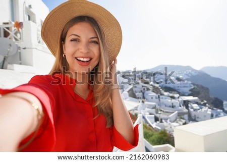 Fashion traveler girl taking selfie photo in Oia picturesque greek village of Santorini Island. Young woman enjoying holidays in Greece, Europe.