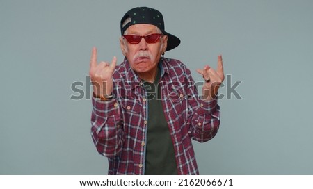 Rock n roll. Overjoyed delighted senior man 80 years old showing gesture by hands, cool sign, shouting yeah with crazy expression, dancing, emotionally rejoicing in success win alone on gray wall