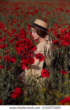 back side of the beautiful girl in yellow dress and hat holding the bouquet of red poppies against of poppy field