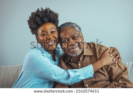 Loving father and daughter together on sofa. Beautiful woman with her father as they both smile. Beautiful young woman embracing her father. Senior African American man and daughter
