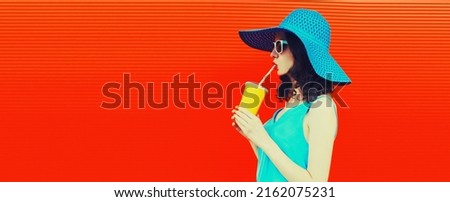 Portrait of beautiful young woman drinking fresh juice from cup wearing summer hat on red background, blank copy space for advertising text