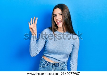 Young brunette teenager wearing casual sweater showing and pointing up with fingers number four while smiling confident and happy. 