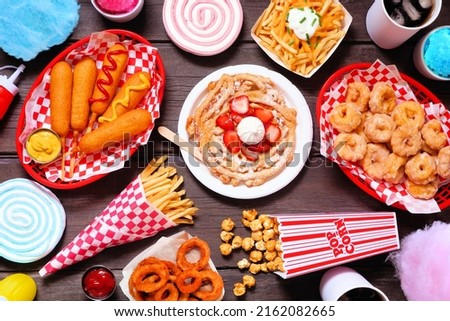 Carnival theme food double border over a dark wood background. Above view with copy space. Summer fair concept. Corn dogs, funnel cake, cotton candy and snacks. Royalty-Free Stock Photo #2162082665