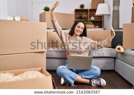 Young hispanic woman using laptop sitting on floor at new home Royalty-Free Stock Photo #2162083587