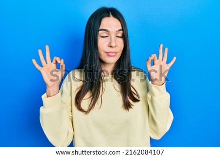 Young brunette woman wearing casual sweatshirt relax and smiling with eyes closed doing meditation gesture with fingers. yoga concept. 