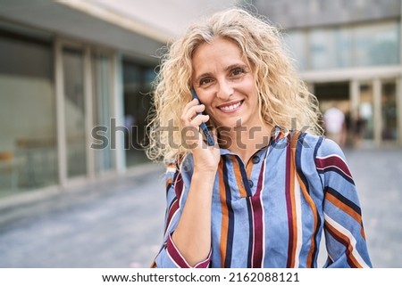Middle age blonde woman smiling confident talking on the smartphone at street