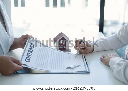 A real estate agent with a house model is talking to clients about buying home insurance and having customers sign contracts under the formal contract agreement. Home rental and insurance concept.
