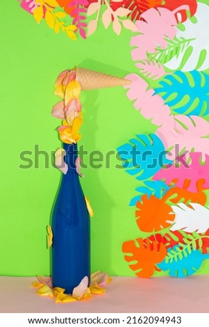 ice cream cone with rose petals melting and falling in a blue bottle on a green background with jungle leaves, creative tropical design