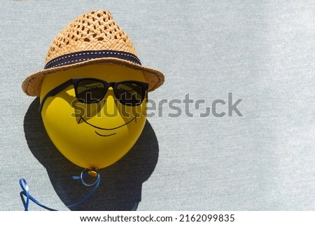yellow balloon with painted face in sunglasses and straw hat on blue background on sunny summer day.  the concept of summer, summer vacation.  copy space.