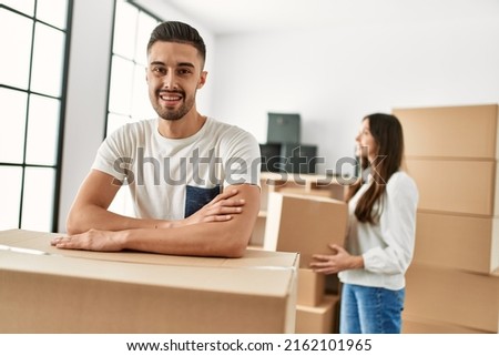 Young hispanic man smiling happy leaning on cardboard at new home.