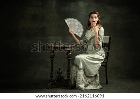 Surprise. shock. Vintage portrait of young beautiful girl in gray dress of medieval fashion style isolated on dark background. Comparison of eras concept, flemish style. Classic art character, old Royalty-Free Stock Photo #2162116091