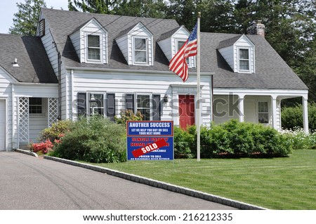 Sold Real Estate (Another Success let Us Help you Buy Sell your Next Home) Sign and American Flag on front yard lawn of Suburban Cape Cod Colonial Style Home Sunny Residential Neighborhood USA
