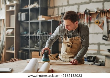 Warm toned portrait of young carpenter sanding wood and building handmade furniture piece in workshop, copy space Royalty-Free Stock Photo #2162132023