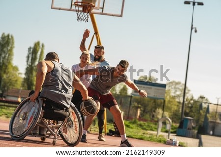 Man in wheelchair play street basketball with his friends.