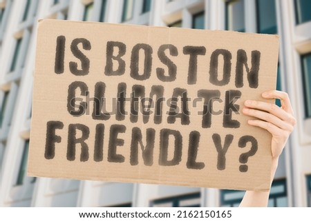The question " Is Boston climate-friendly? " is on a banner in men's hands with blurred background. Support. Team. Activist. Urban. Sunset. Carbon. Ecology. Energy. New. Clean. Warming. Waste