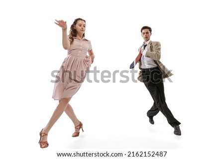 Young man and woman in vintage retro style outfits dancing social dance isolated on white background. Timeless traditions, 1960s american fashion style and art. Dancers look happy, delighted