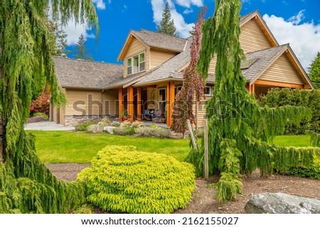 Craftsman home cedar siding solid wood pillars patio veranda deck grassy green yard blue sky and landscaping