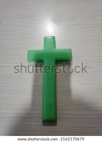 a green jade cross displayed on a wooden patterned wall