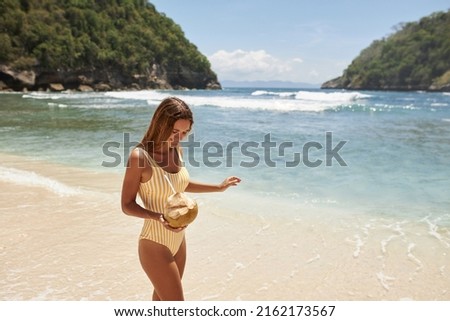 Beautiful girl in a yellow swimsuit with a coconut in her hands on the beach. Girl in a yellow bikini, resting on a deserted beach in Bali