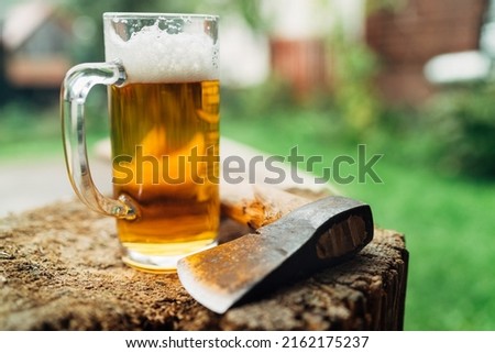 Still lifephoto of glass of fresh cold beer on wooden stub alongside axe. Rural concept, masculinity, coarse, rough wilderness lifestyle concept.	 Royalty-Free Stock Photo #2162175237